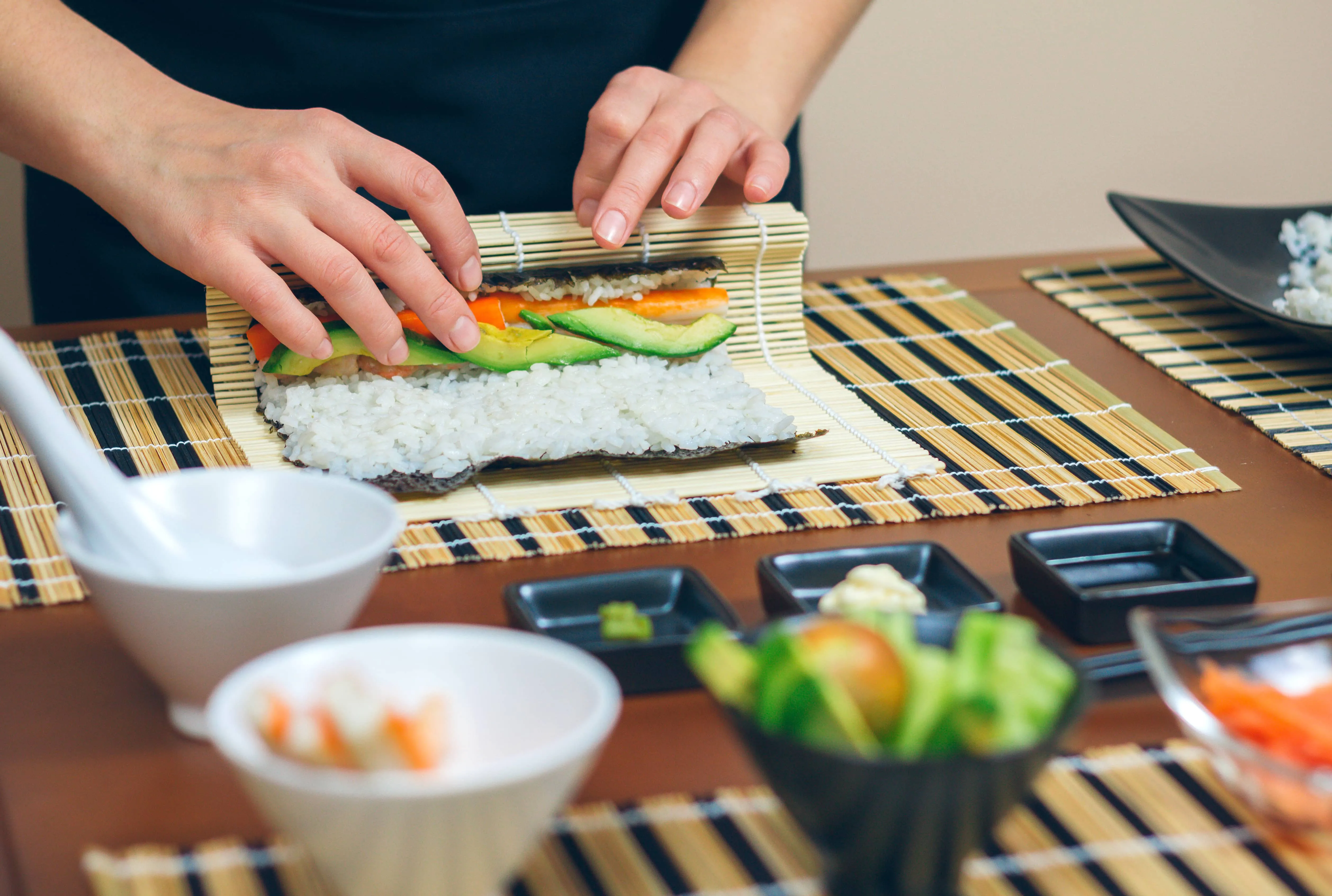 Close-up of hands rolling fresh sushi with avocado and vegetables using a bamboo mat